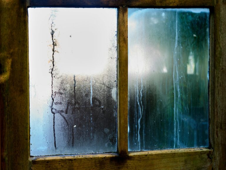 Condensation and water streaks on an old wooden window caused by moisture collecting on cold glass.