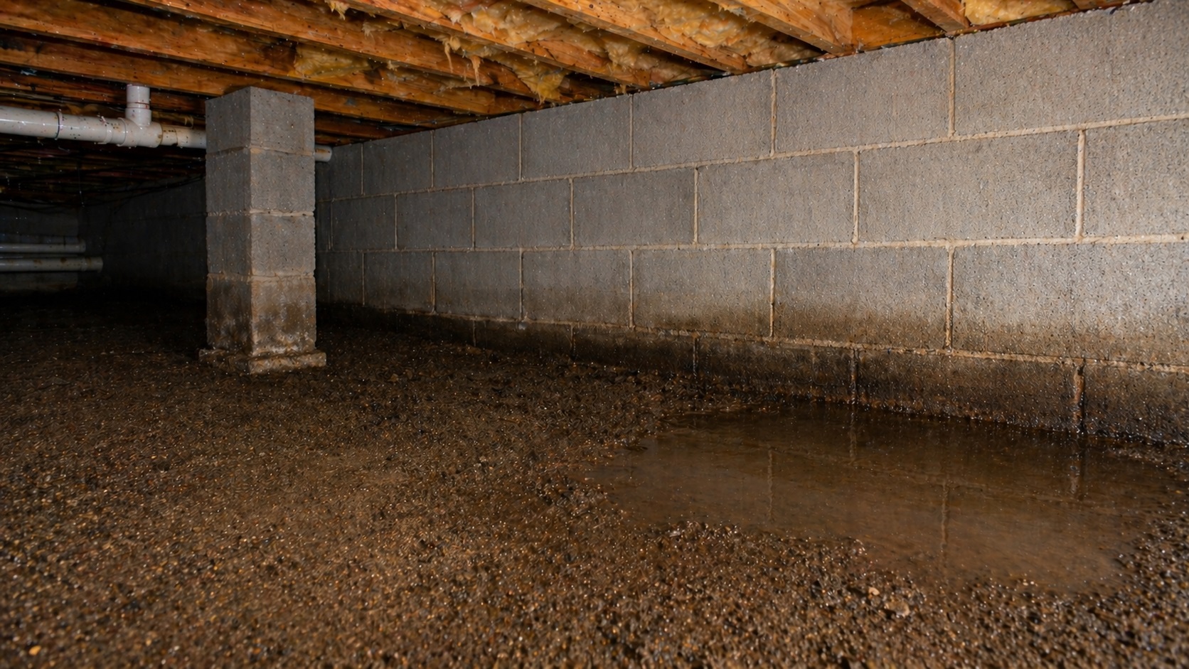 Damp crawl space with wet soil and shallow puddle along foundation wall showing ground moisture problem