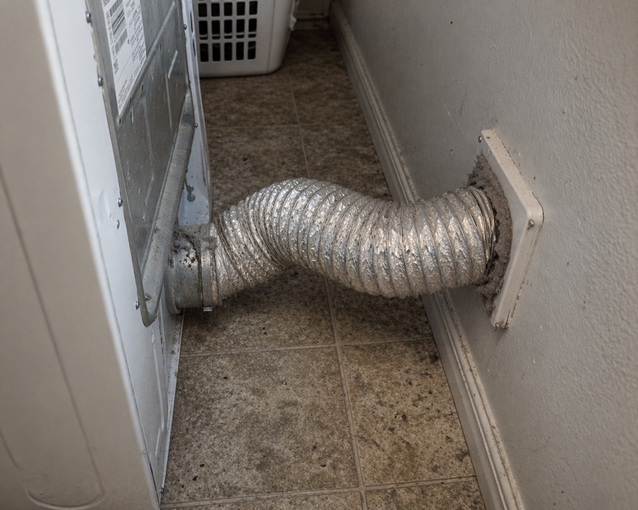 Dryer vent hose connected behind residential clothes dryer in laundry room
