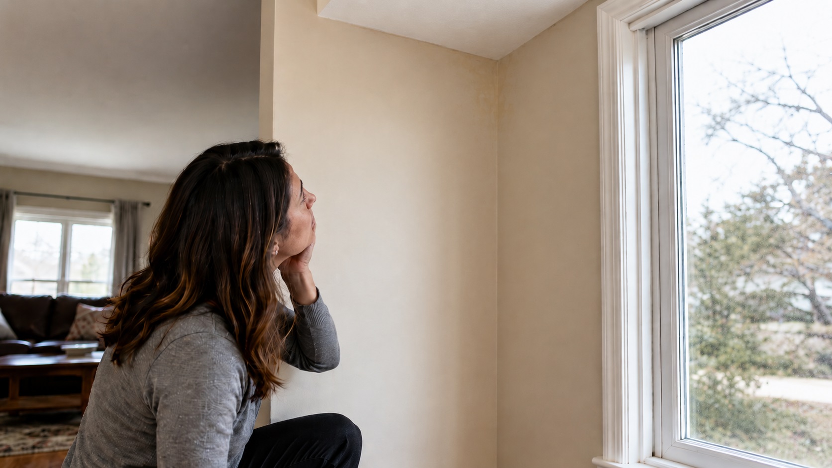 Homeowner inspecting subtle water stains near the ceiling and upper wall by a window