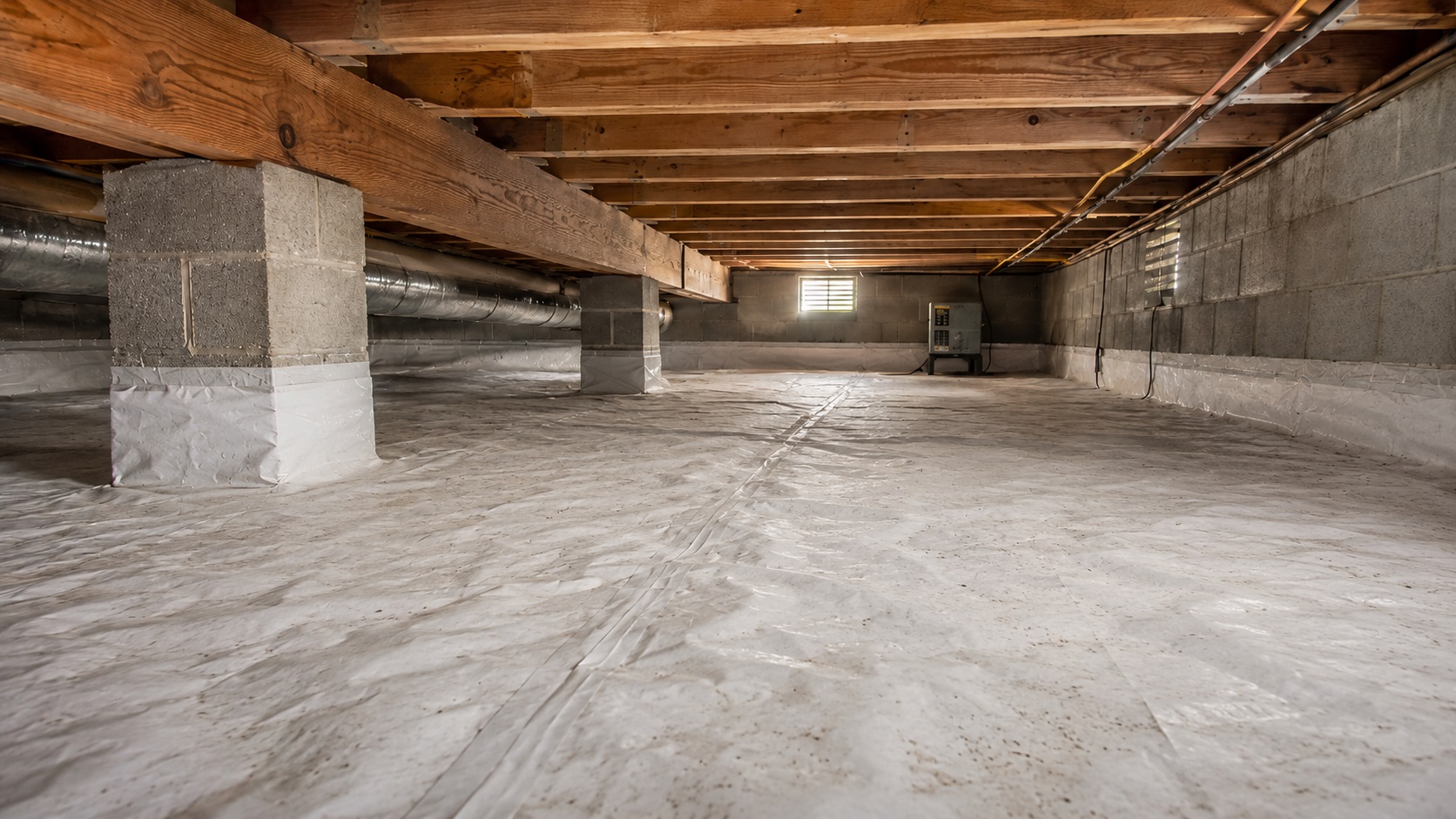 Clean crawl space with a sealed vapor barrier, dry wood joists, block piers, ductwork, and a small dehumidifier for moisture prevention.