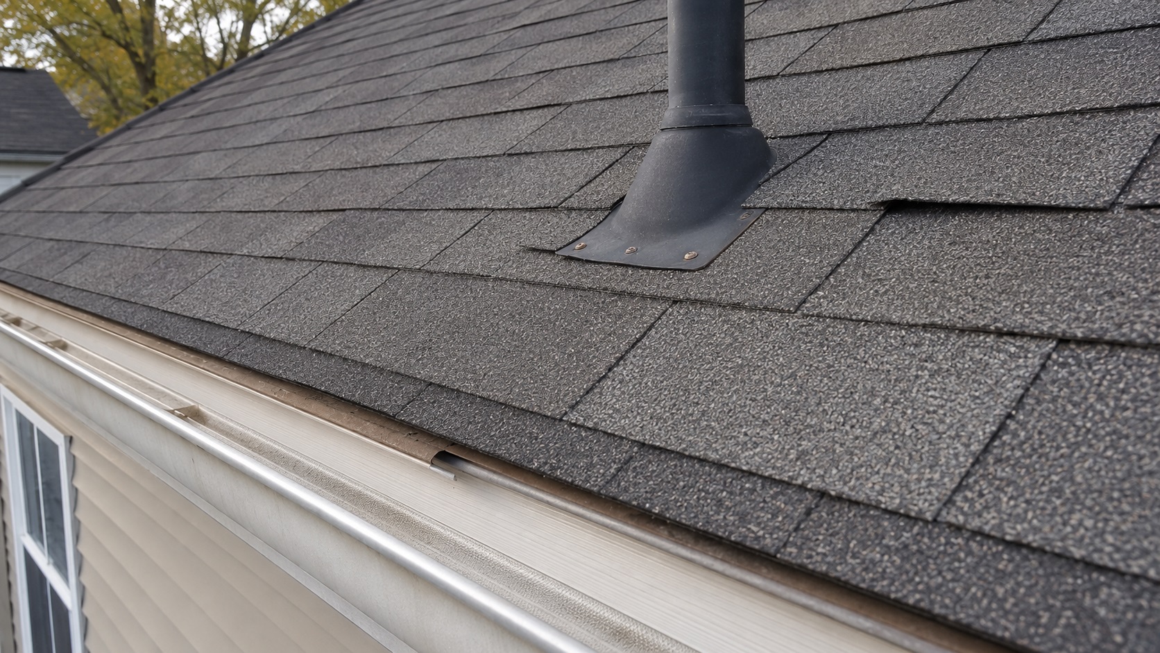Close-up of an asphalt shingle roof showing a poorly installed vent boot, uneven shingle alignment, and an exposed nail near the roof edge.