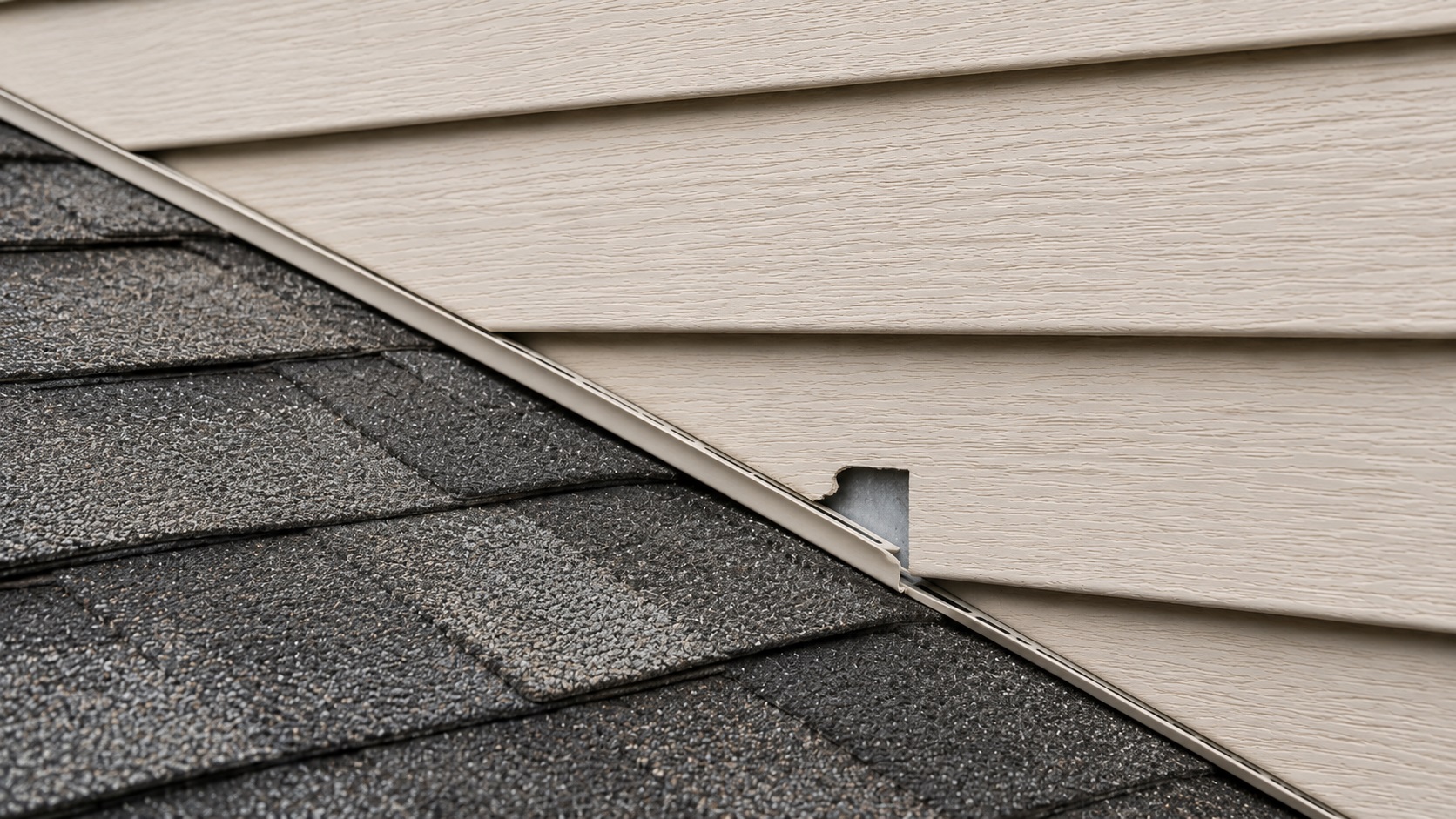 Cracked siding and J-channel above a roof edge exposing flashing at a roof-to-wall junction
