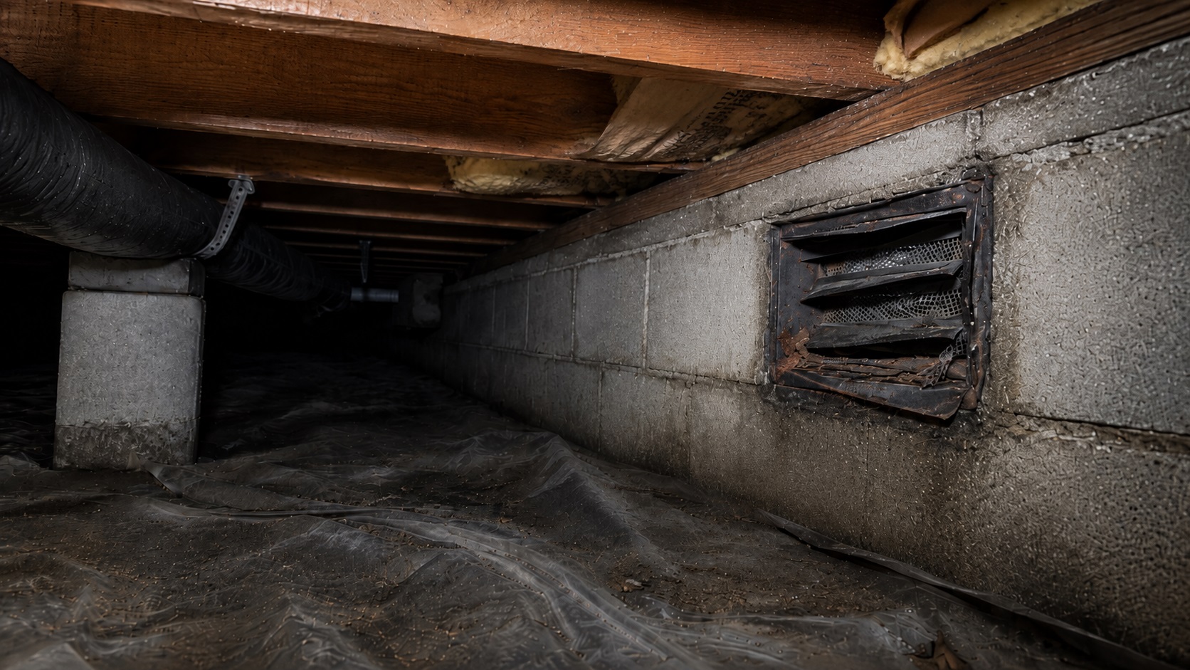 Damaged crawl space foundation vent with bent louvers, torn screen, debris, damp wall staining, joists, insulation, ductwork, and vapor barrier.