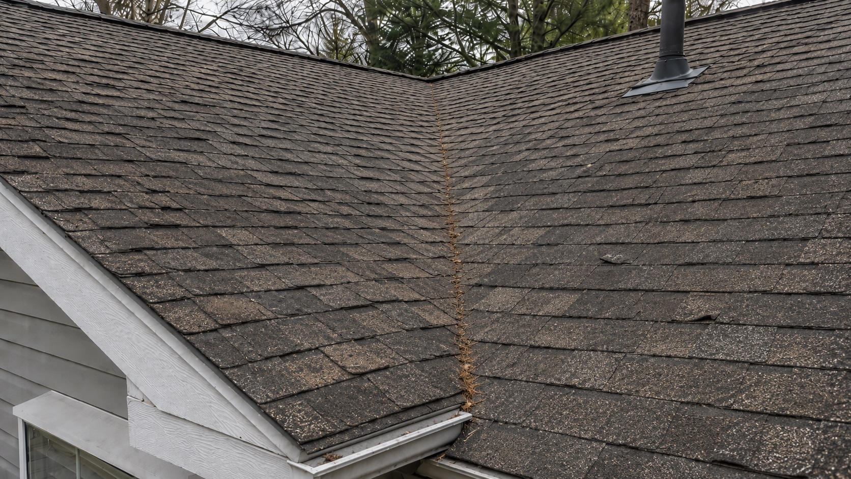 Aging asphalt roof with faded shingles, granule loss, lifted edges, and light debris collecting in a worn roof valley.