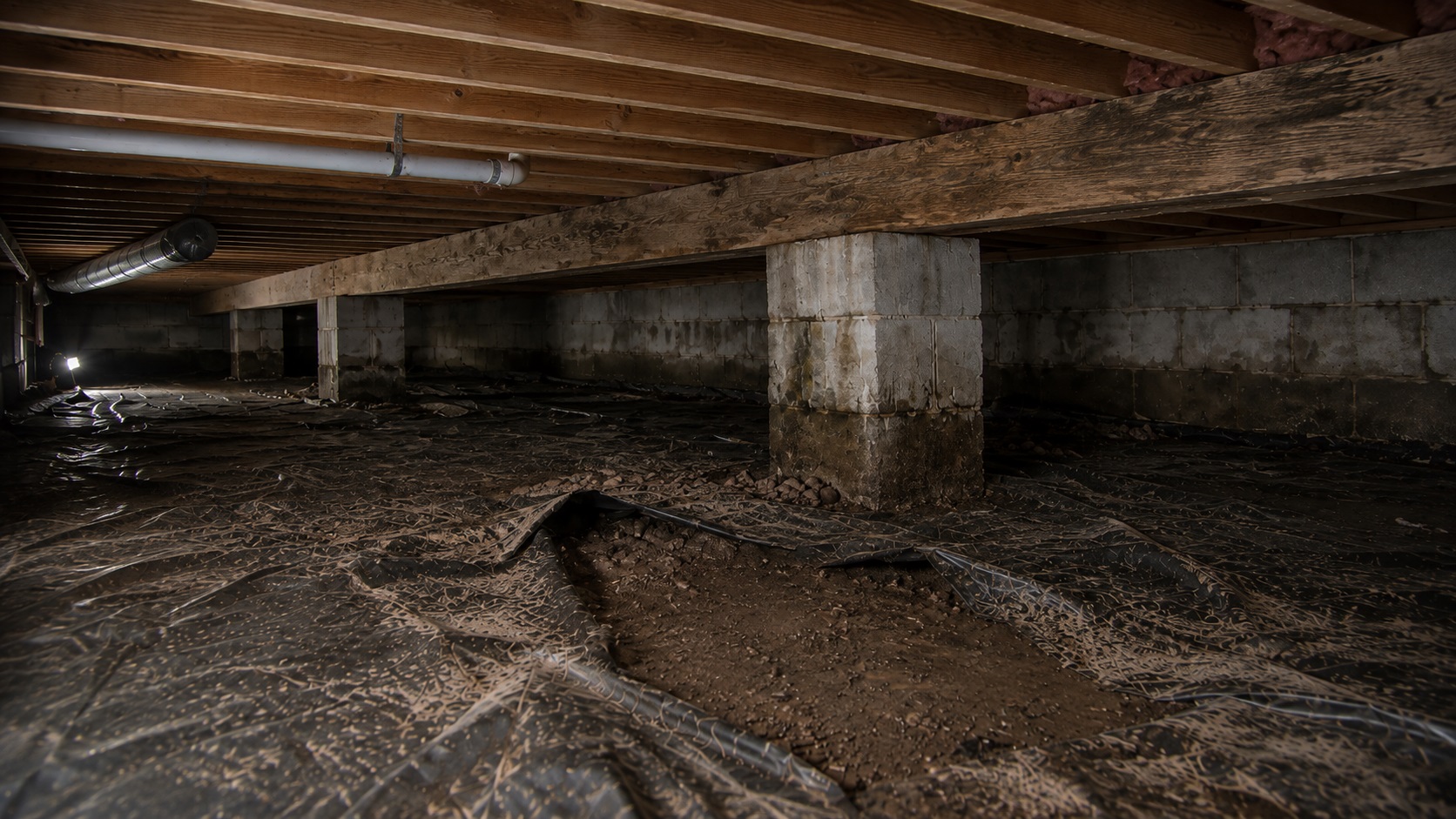 Damp crawl space with a torn vapor barrier, exposed soil, stained block pier, wood beam, joists, pipes, and ductwork showing signs that encapsulation may be needed.