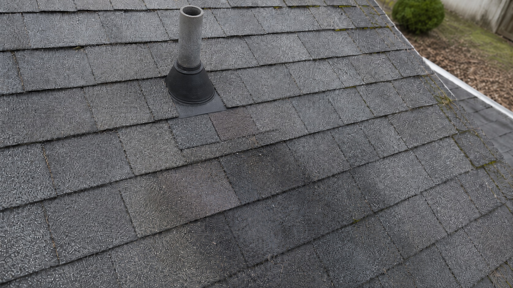 Open plumbing vent pipe on a weathered asphalt-shingle roof with mismatched repair shingles and damp staining below the vent boot.